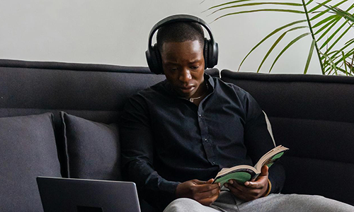 Man reading a book with headphones on.