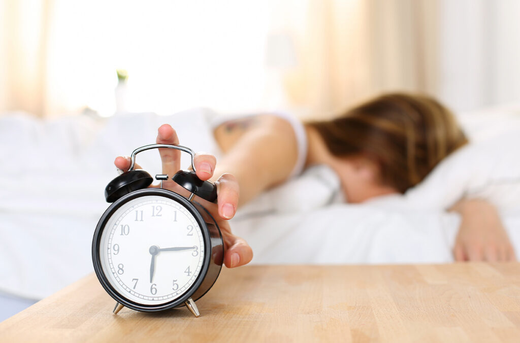 Clock on a table with woman sleeping in backgrouns